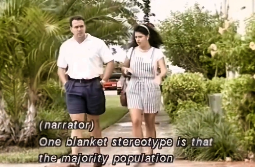 A man and a woman walking outdoors on a path surrounded by tropical plants. Text: One blanket stereotype is that the majority population is responsible for most stereotyping of others.