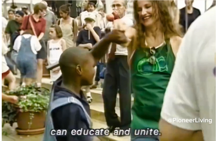 A woman smiling and reaching toward a young boy in a blue shirt, with a crowd of people in the background. The text 'can educate and unite.'